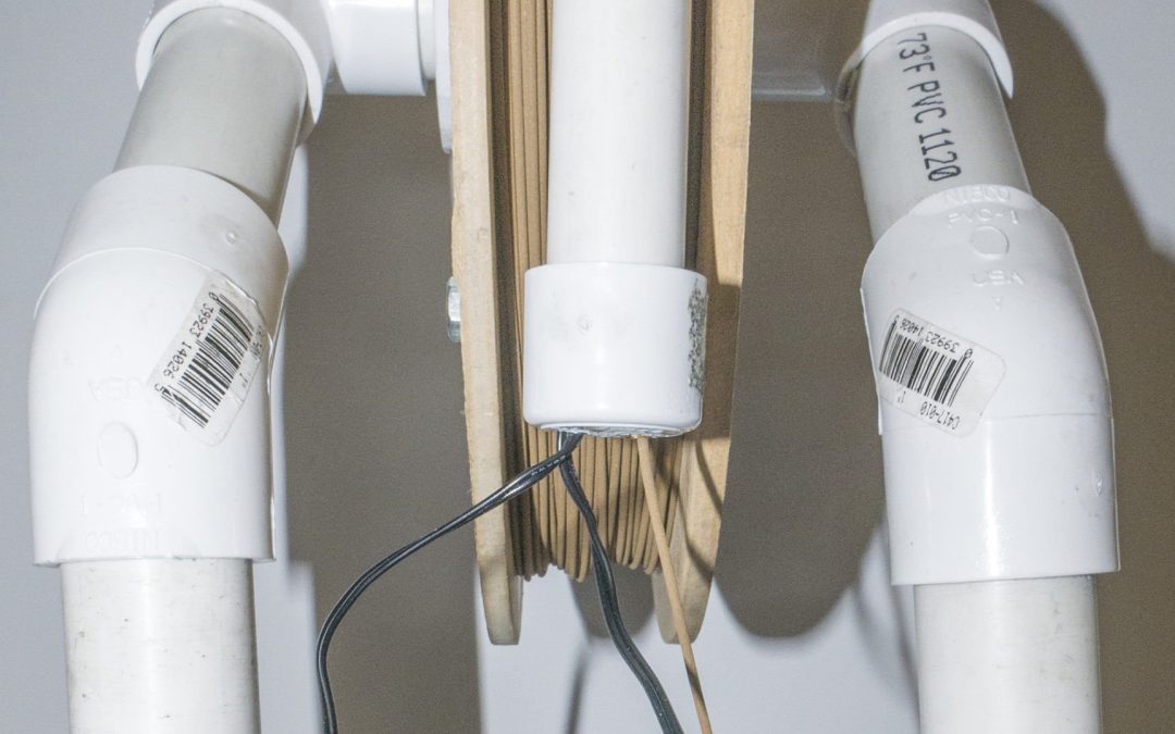 PVC piping and wooden spool with filament, illustrating components of a 3D printing setup for metal filaments.