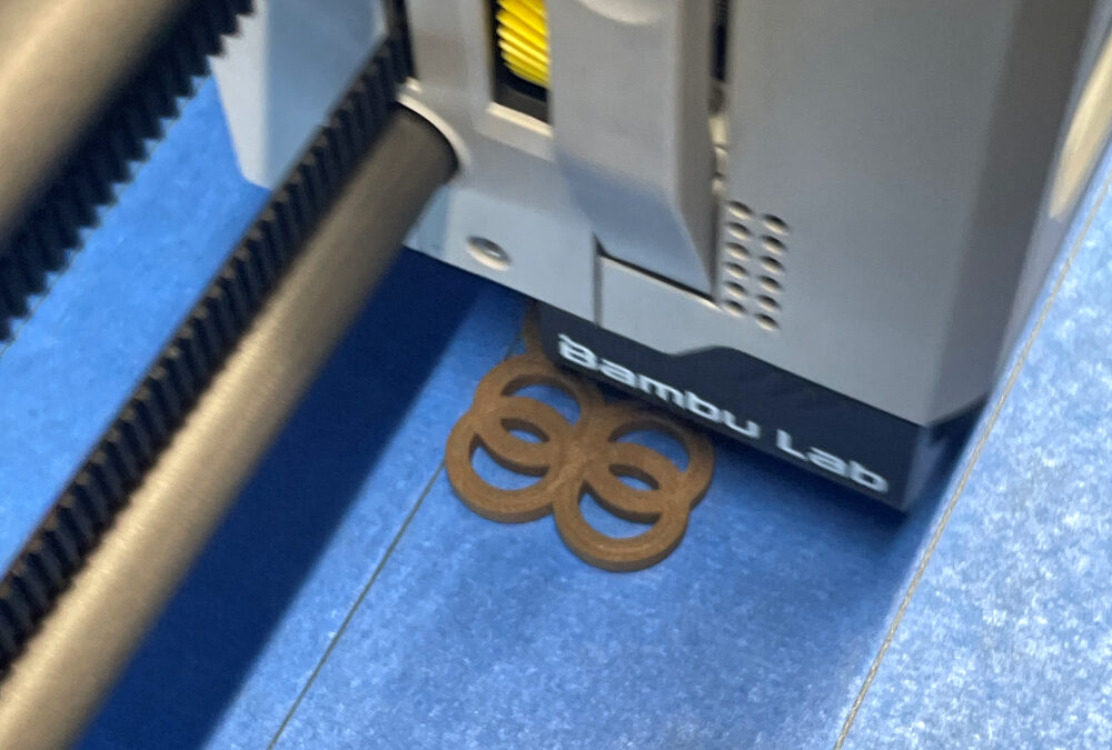 Bambu Lab 3D printer with freshly printed metal filament part on blue surface, highlighting innovations in #FFFmetal 3D printing technology.