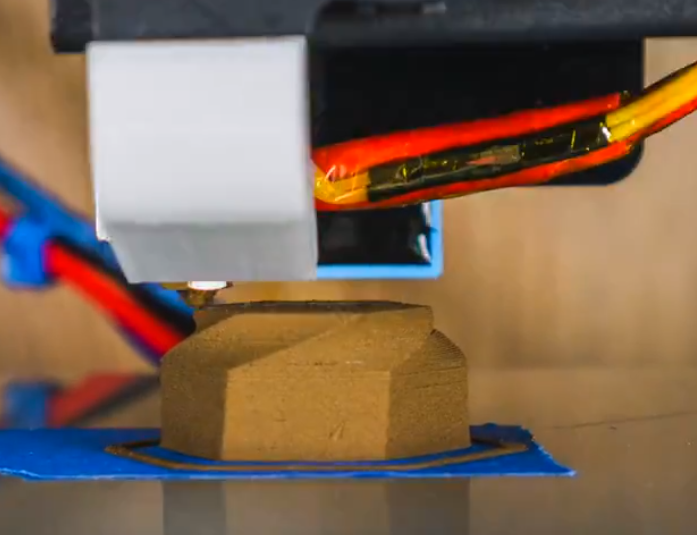 3D printer nozzle extruding metal filament onto a blue print bed, showcasing the additive manufacturing process for metal parts.
