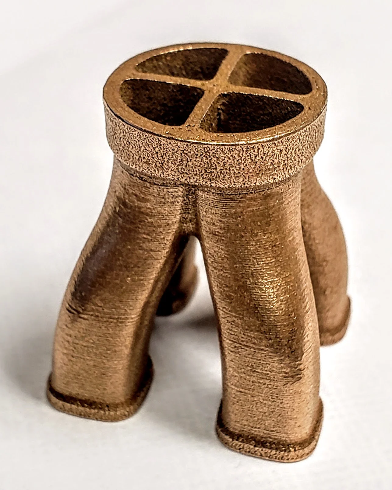 Metal 3D printed part showcasing Filamet™ material, featuring a unique design with a circular top and four supporting legs.