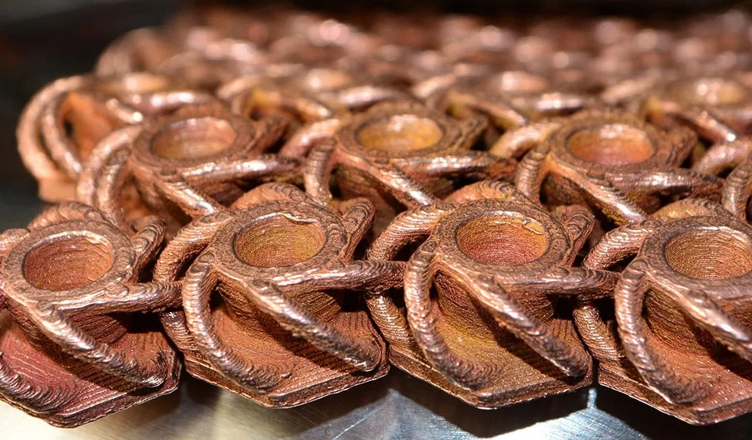 Close-up of intricately designed FFF metal 3D printed parts, showcasing copper-like filament textures and details, relevant to Bambu Lab's innovations in affordable metal prototyping.